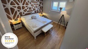 Een slaapkamer met een modern design, met een bed met witte lakens, een houten hoofdeinde en een nachtkastje met een lamp.