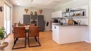 Een moderne keuken met een centraal kookeiland, houten vloeren en een eethoek met twee stoelen.
