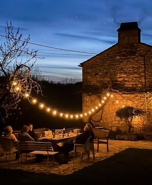 An outdoor dining area with stone walls, string lights, and a stone building in the background. - Romantische wijnboerderij met zwembad, buitenkeuken en pizza-oven. (Veyrines-de-Domme)