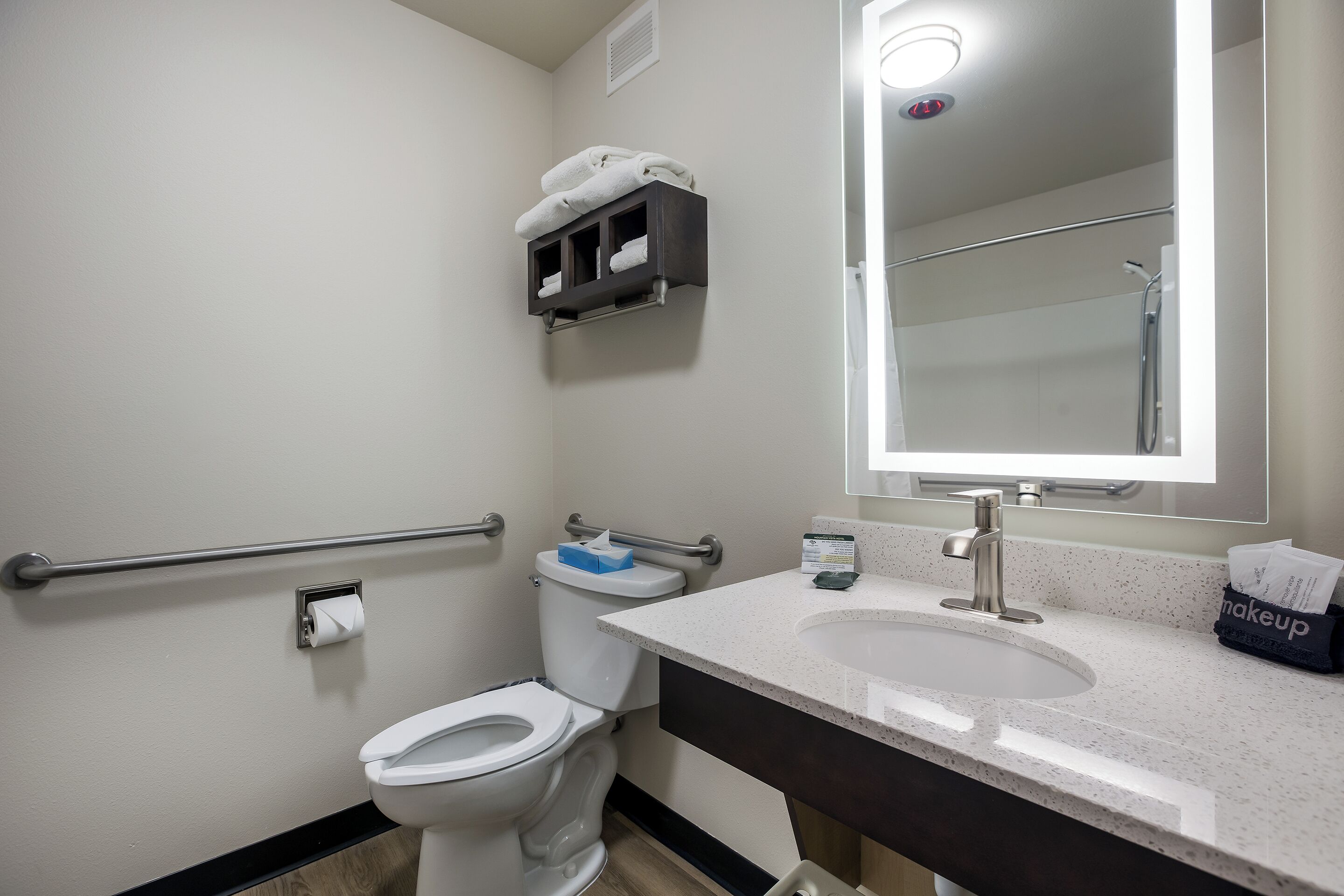 Un bagno con il water bianco, un lavandino con specchio e un portascopevoli sopra il water.
