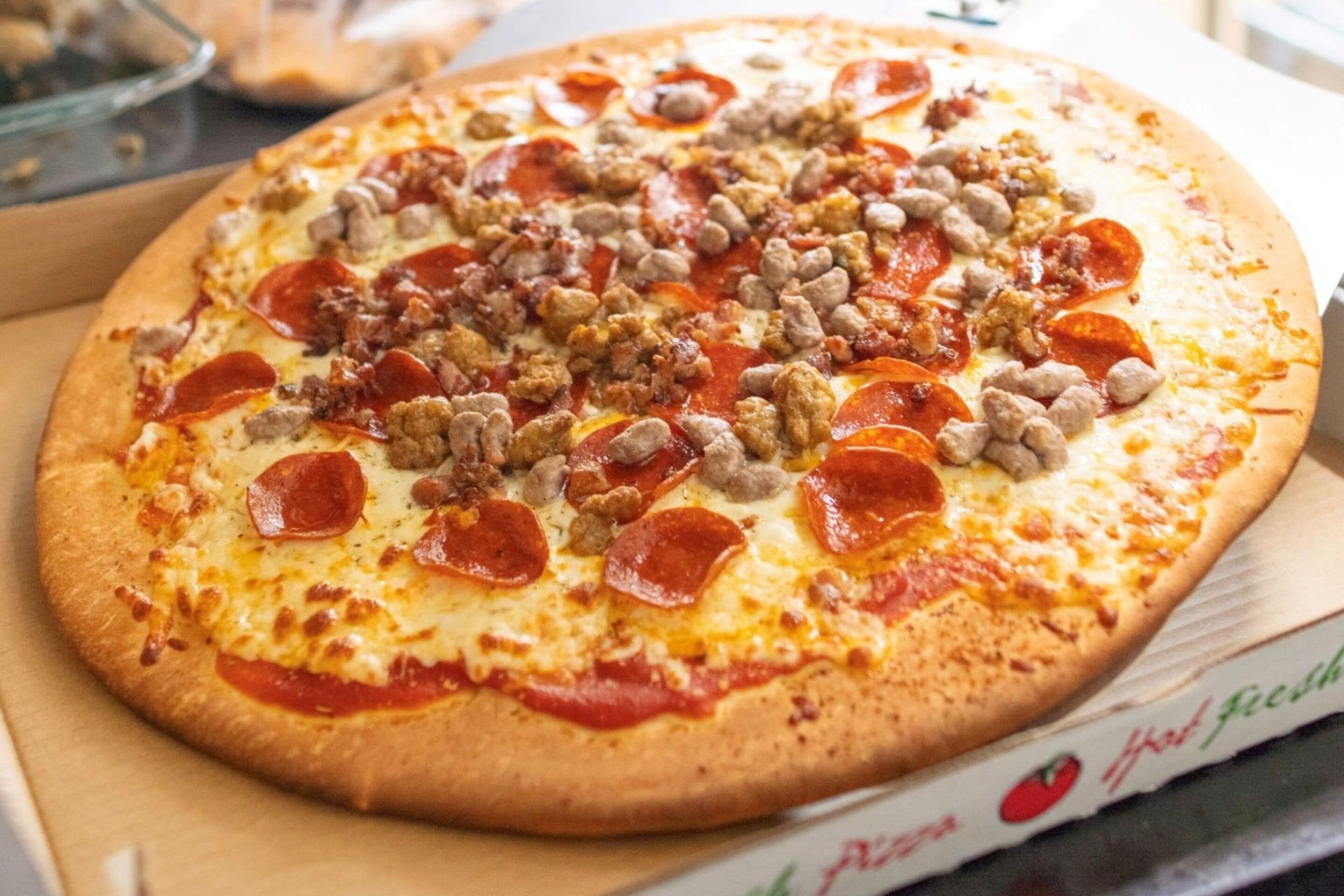 Una pizza con pepperoni y salchicha en una caja.