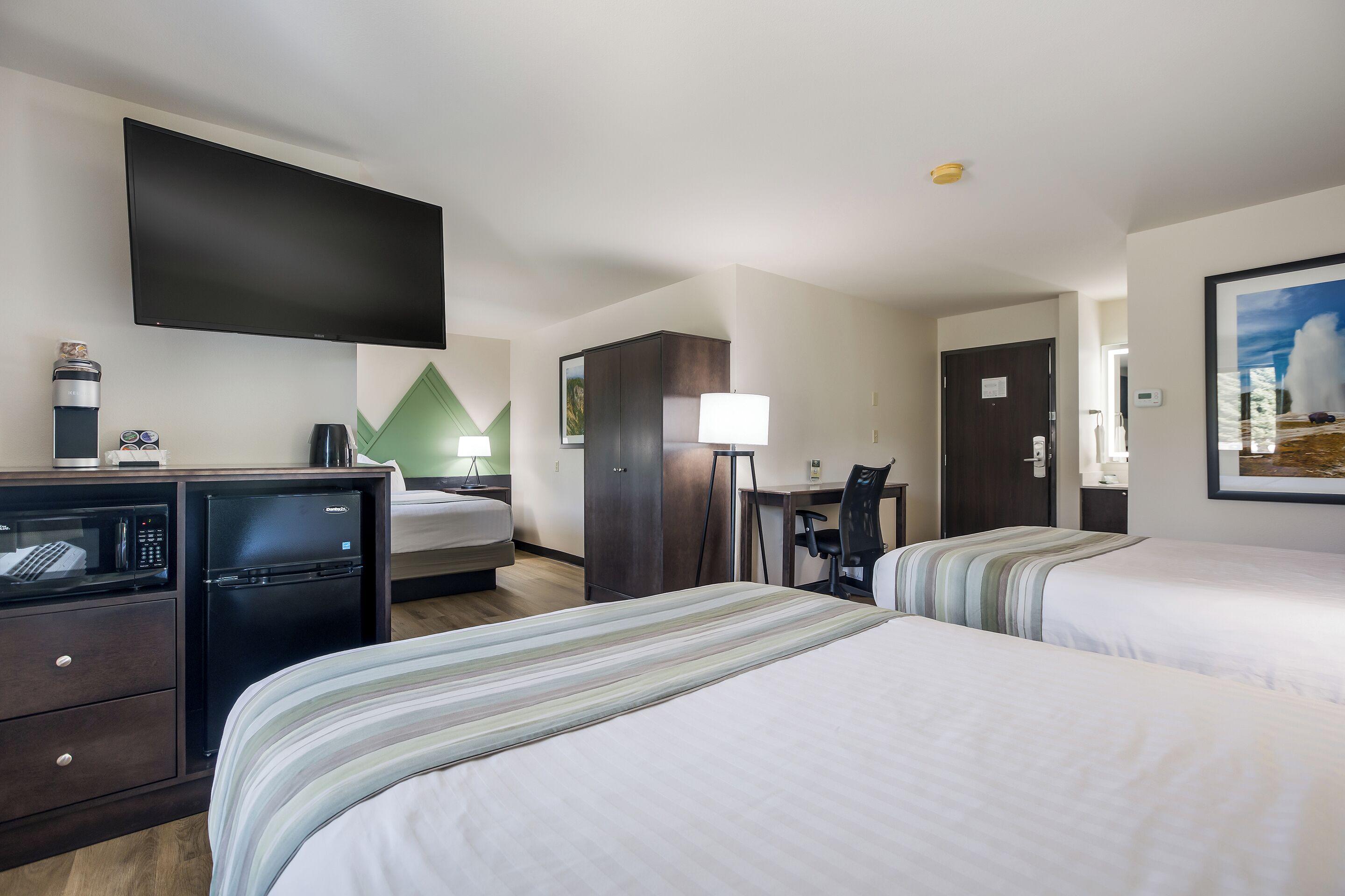 A hotel room with two beds, a desk, a television, a minibar, and a desk lamp.