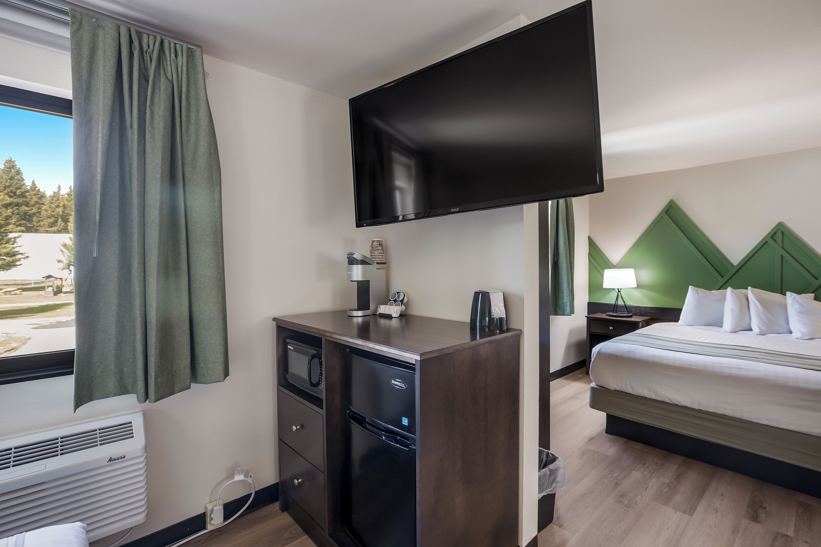 Une chambre d’hôtel équipée d’un lit, d’un bureau avec un téléviseur à écran plat, d’un mini-réfrigérateur, d’une machine à café et d’une fenêtre avec des rideaux.