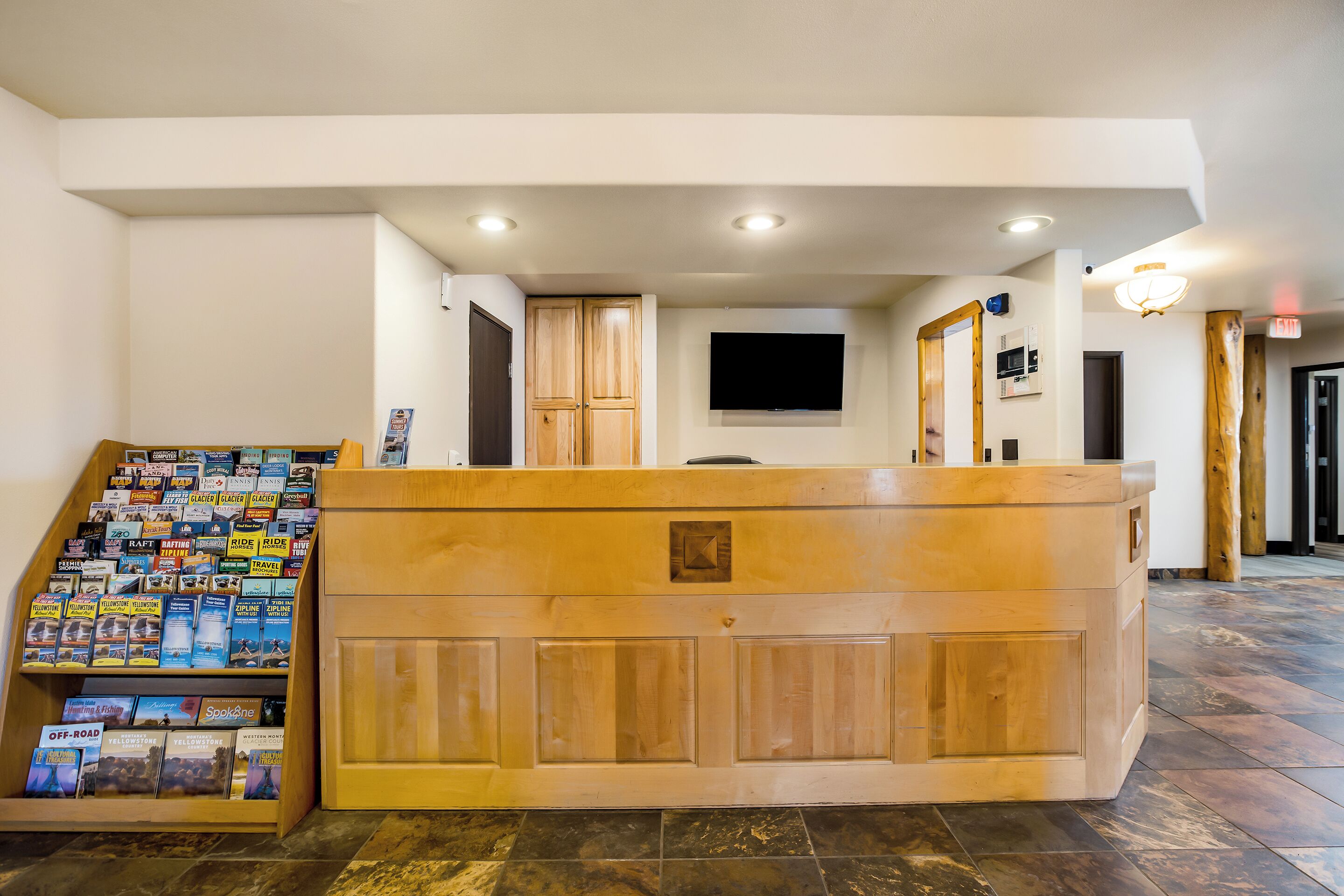 A reception area with a wooden counter, a display of travel brochures, and a flat-screen TV mounted on the wall.
