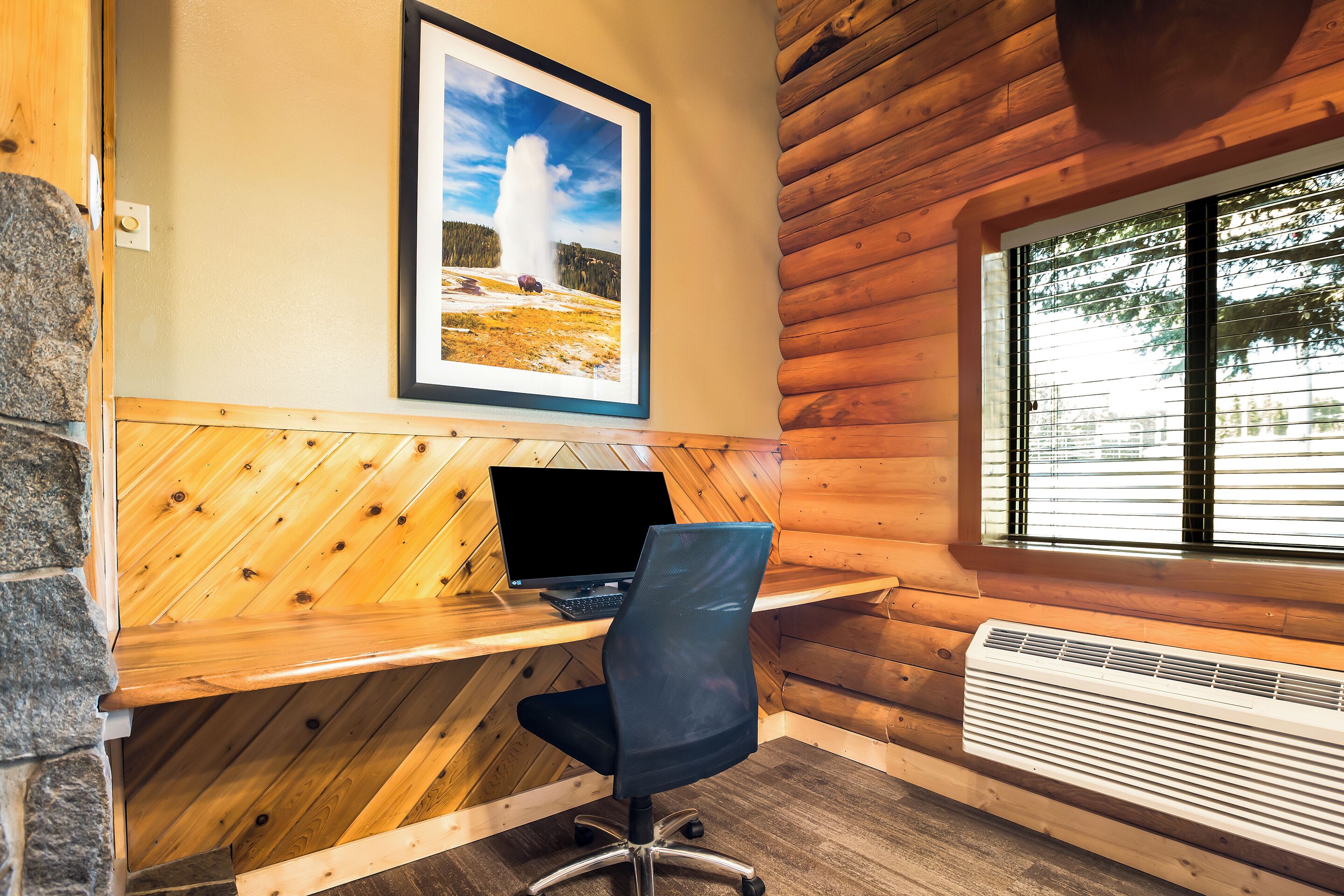 A wooden cabin interior with a desk, chair, and a framed picture of a geyser.