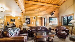 A log cabin interior with a wooden ceiling, leather furniture, and a fireplace.