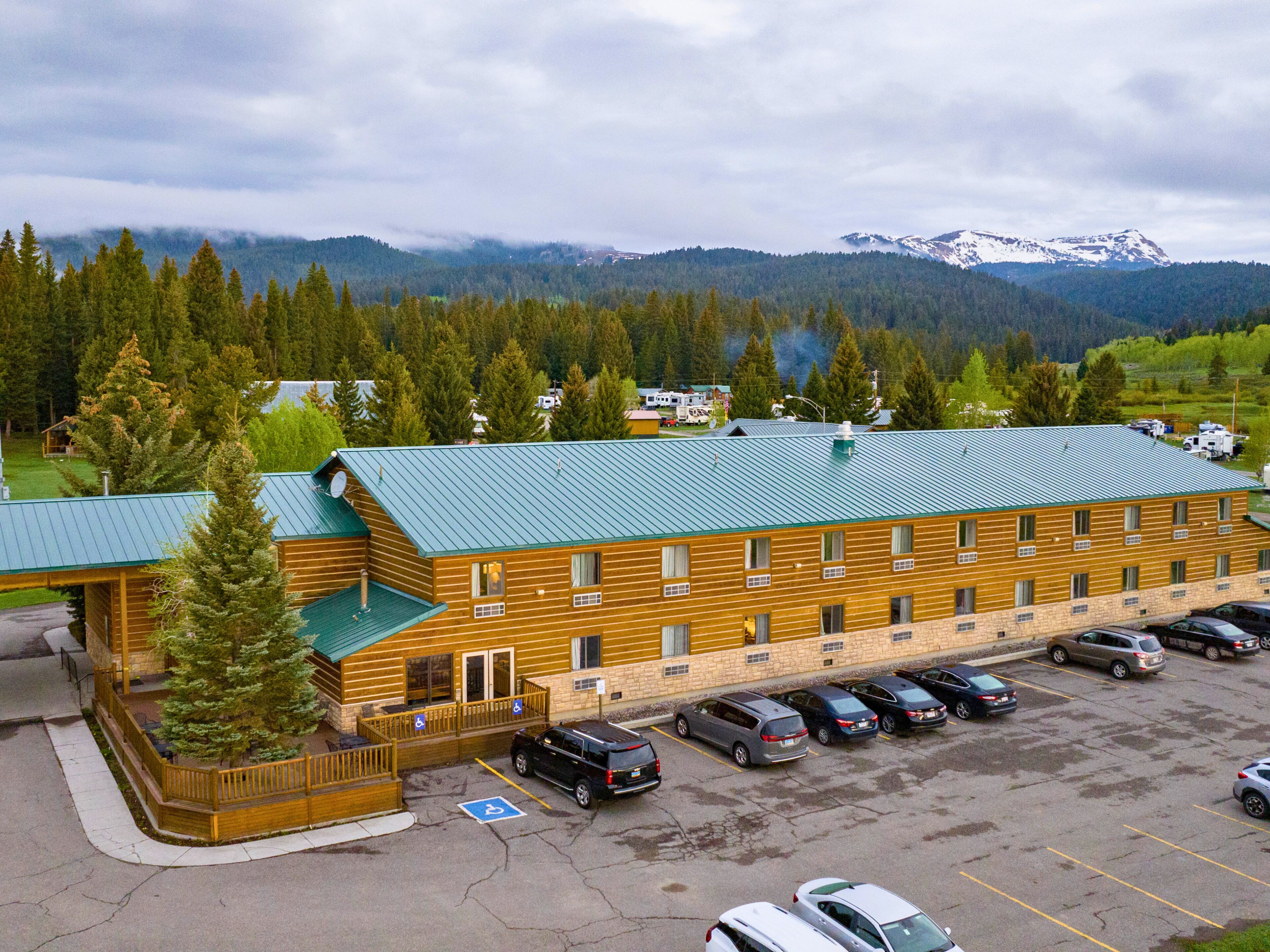 A multi-story lodge with a green roof, parking lot, and a mountainous backdrop.