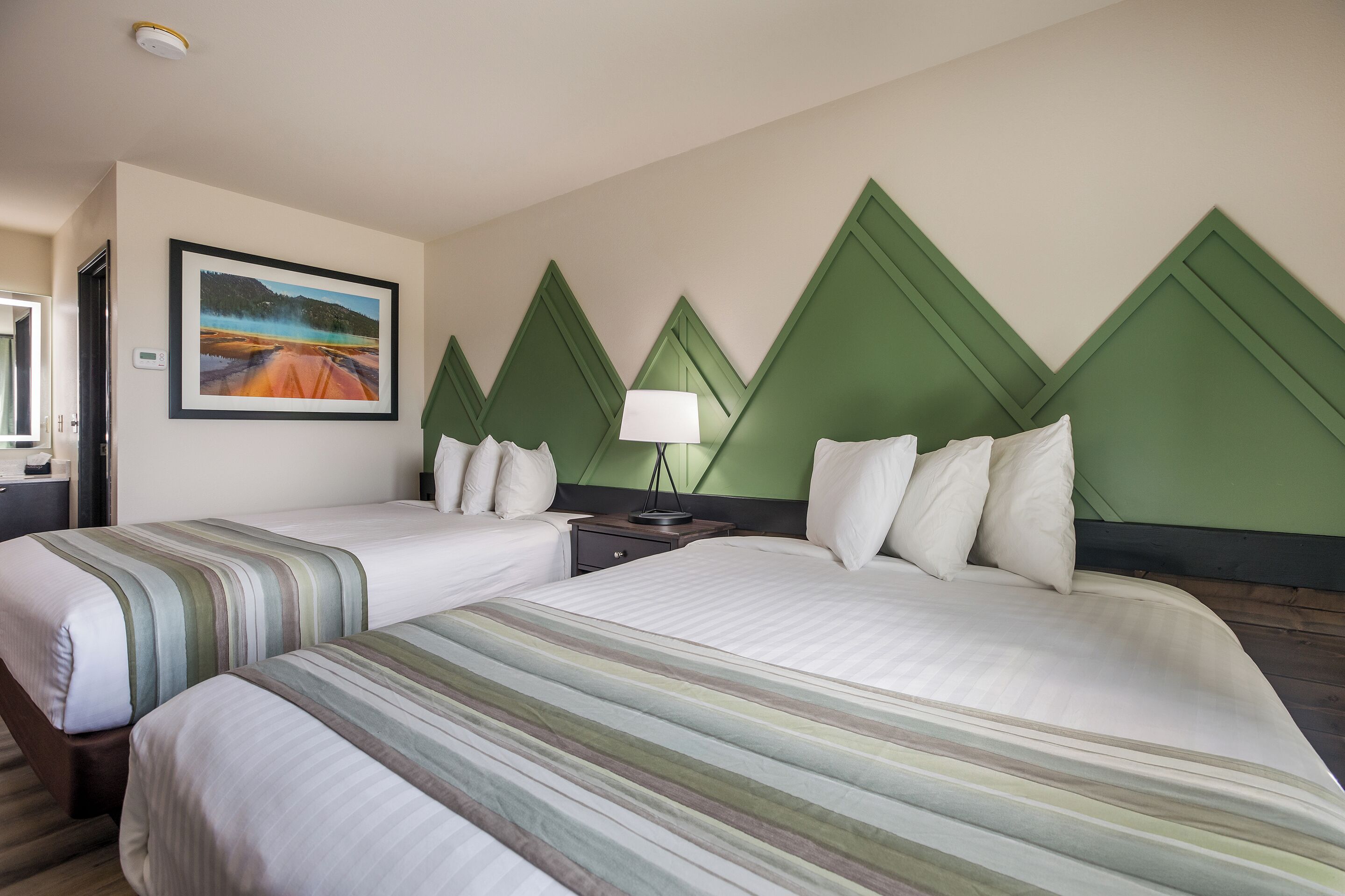 Una habitación de hotel con dos camas, una mesita de noche, una lámpara y un cuadro en la pared.