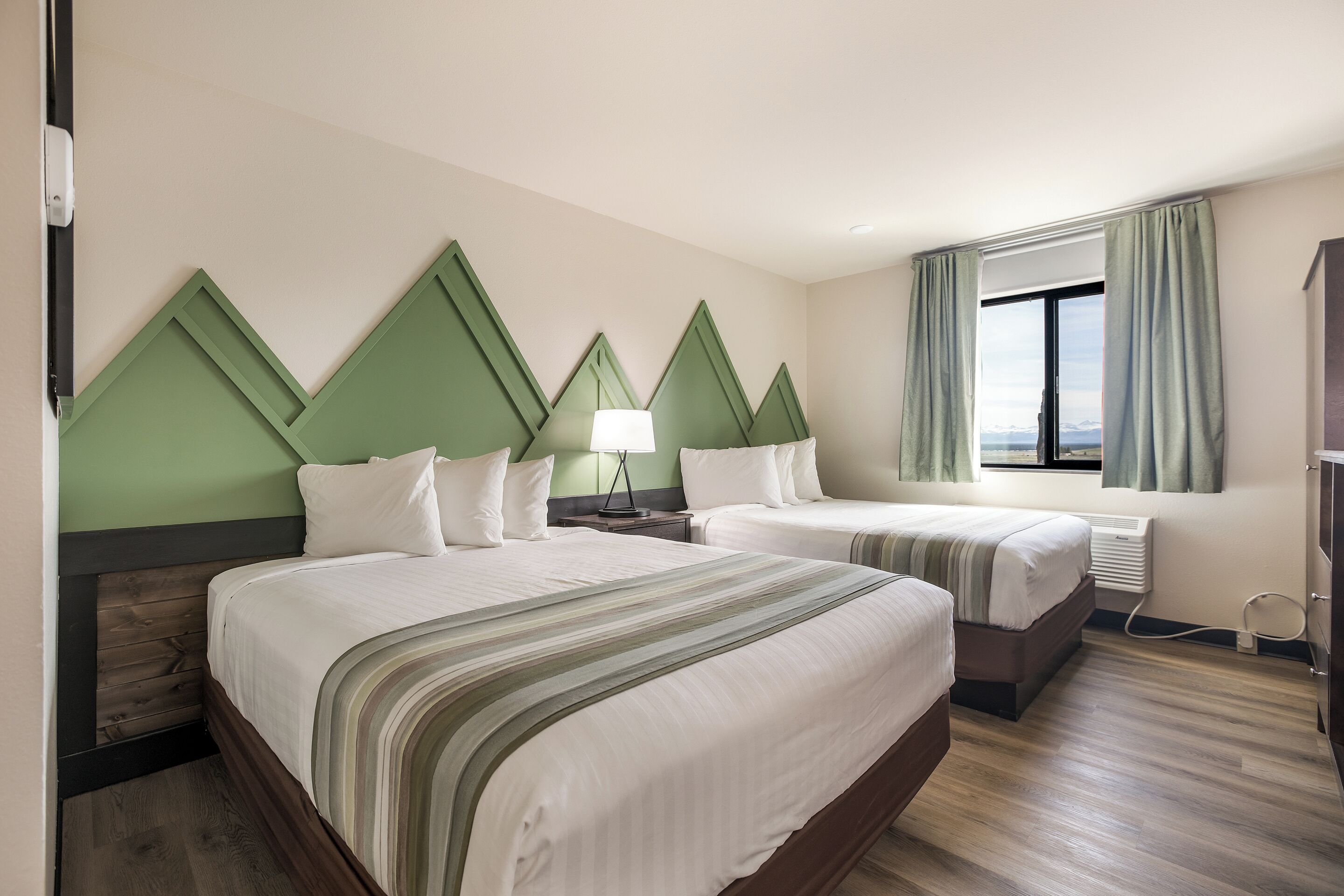A hotel room with two beds, a window with curtains, and a view of the mountains.