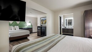 A hotel room with a bed, a desk, a TV, a painting, and a bathroom visible through an open door.