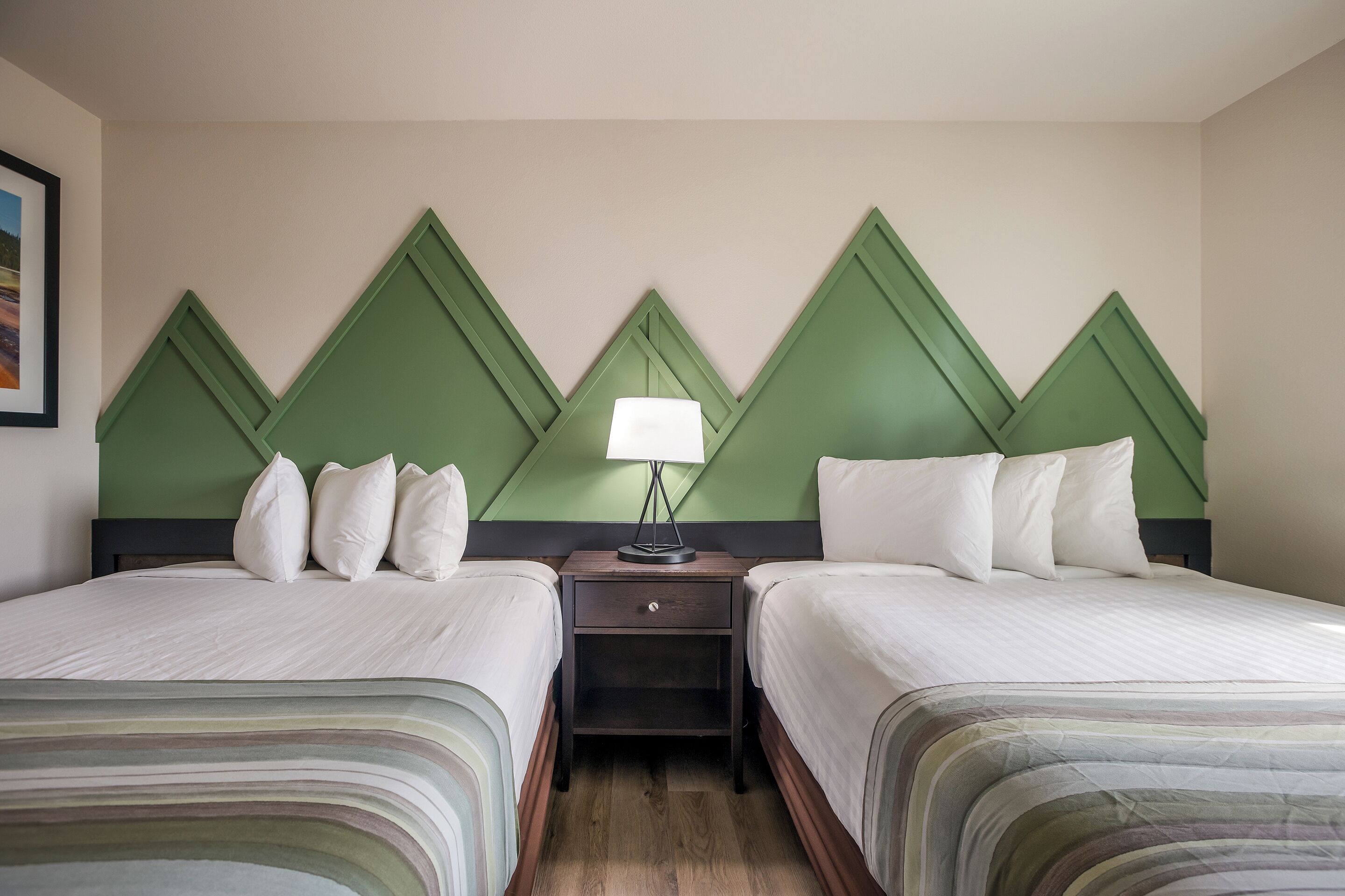 Une chambre d’hôtel avec deux lits, une table de chevet avec une lampe et un mur d’accent vert.
