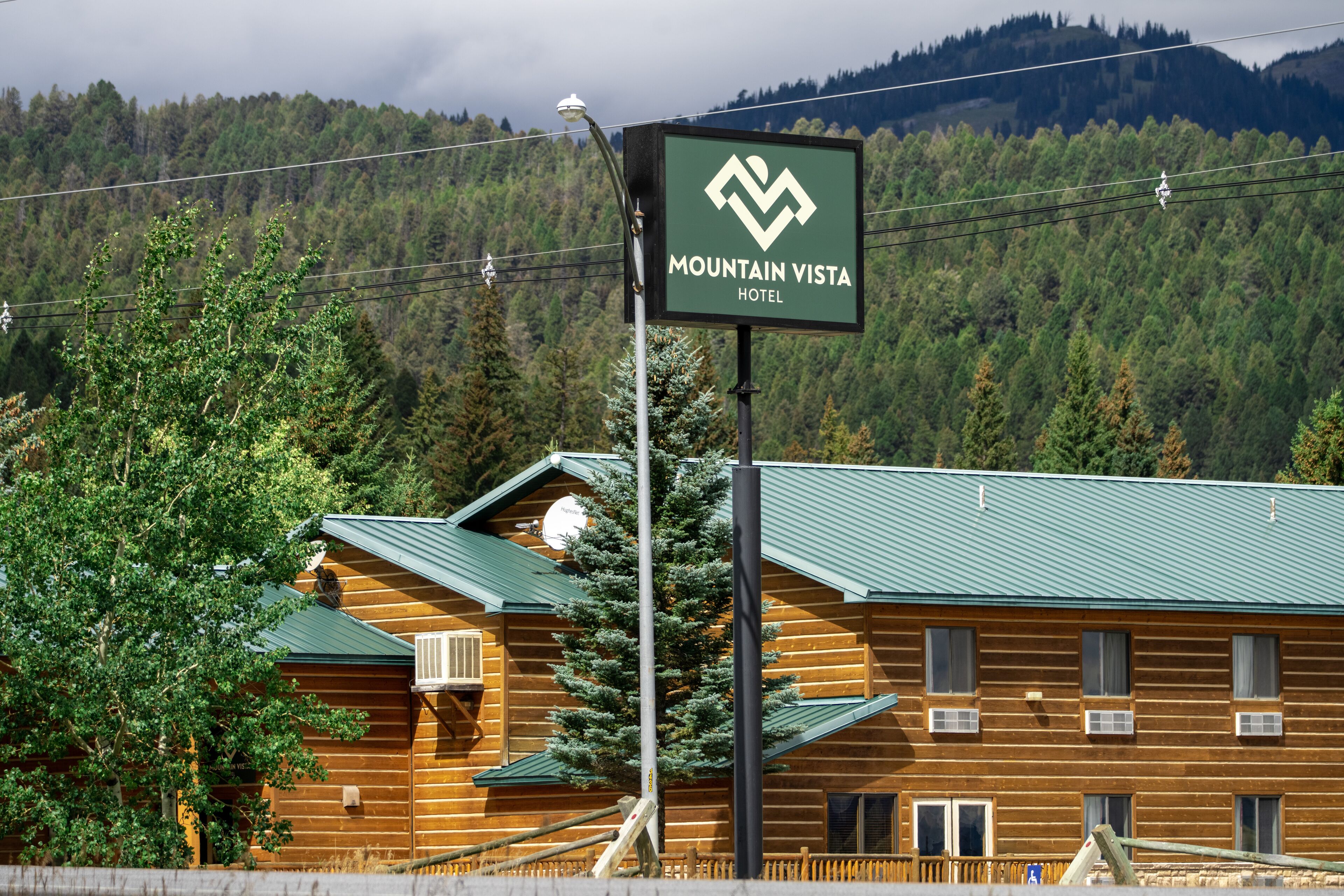 A Mountain Vista Hotel with a prominent sign, wooden log cabin structure, and a forested mountain backdrop.
