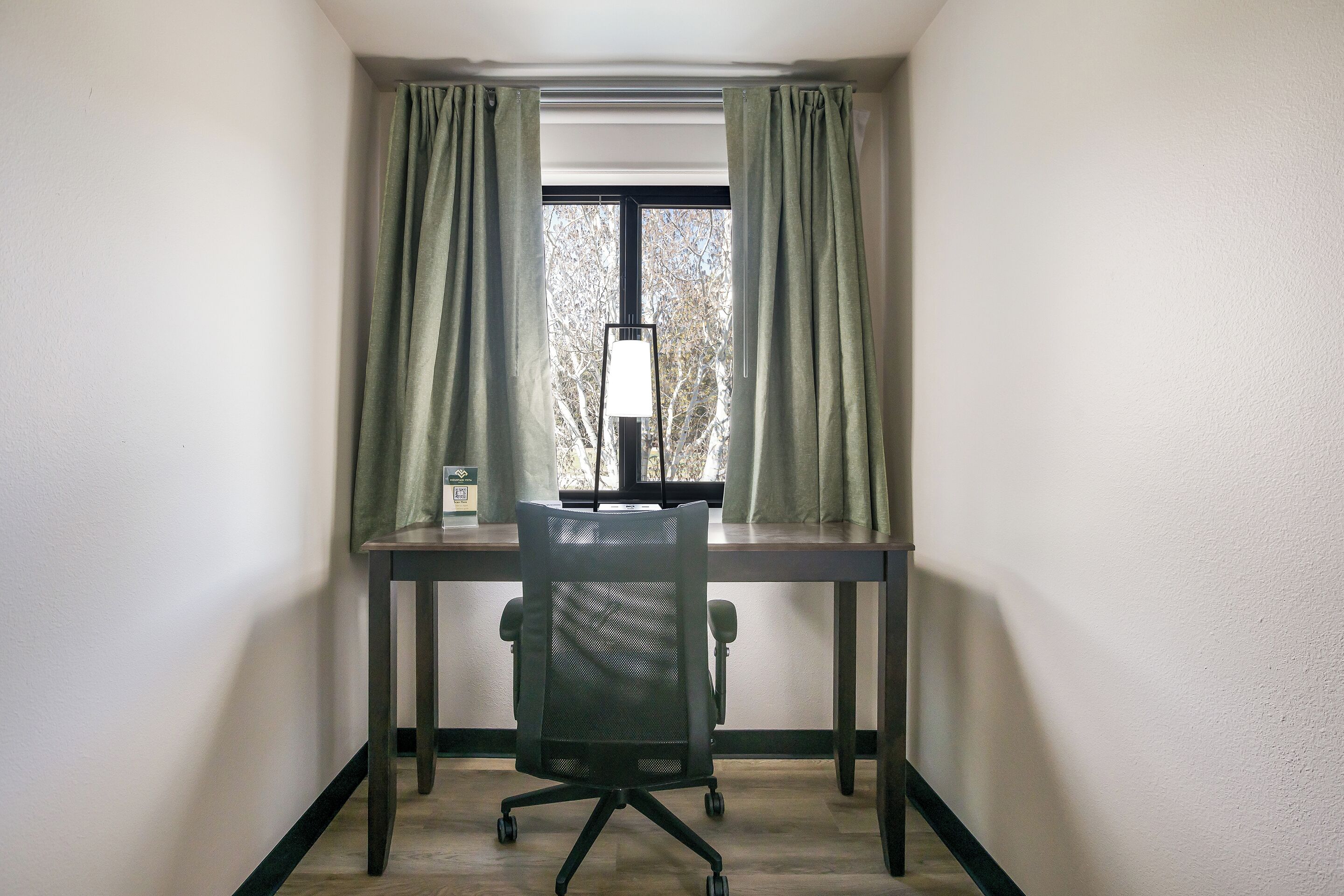 Ein Büro mit Ecke, Schreibtisch, Stuhl und einem Fenster mit Vorhängen.
