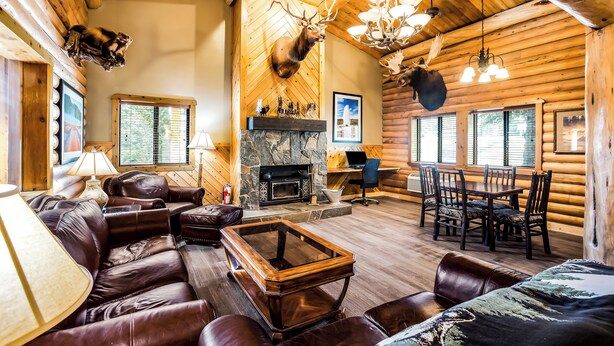 A log cabin interior with a fireplace, leather furniture, and mounted animal heads.