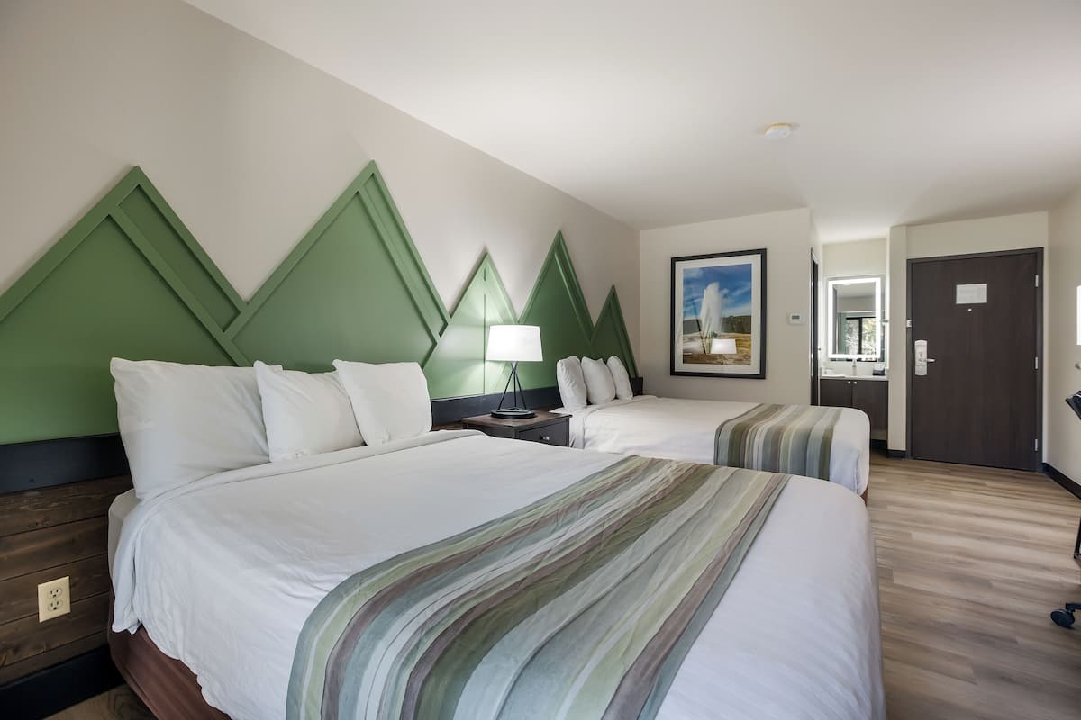 Een hotelkamer met twee bedden, een nachtkastje, een lamp en een lijst aan de muur.