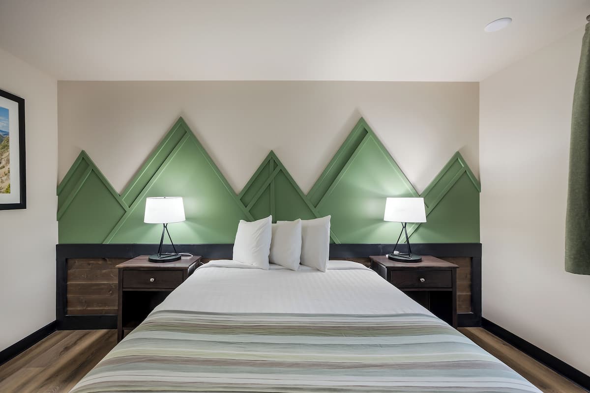 Een hotelkamer met een groot bed, twee nachtkastjes met lampen, en een groene accentmuur.