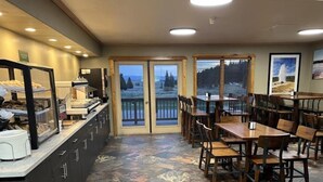 A restaurant with a counter, dining tables, chairs, and a view through the glass doors.