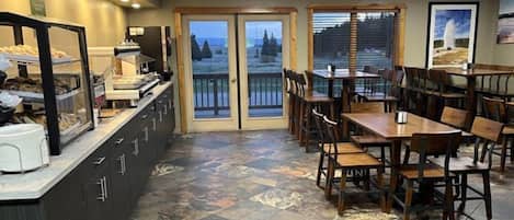 Un restaurante con mostrador, mesas, sillas y vistas a través de puertas de cristal.