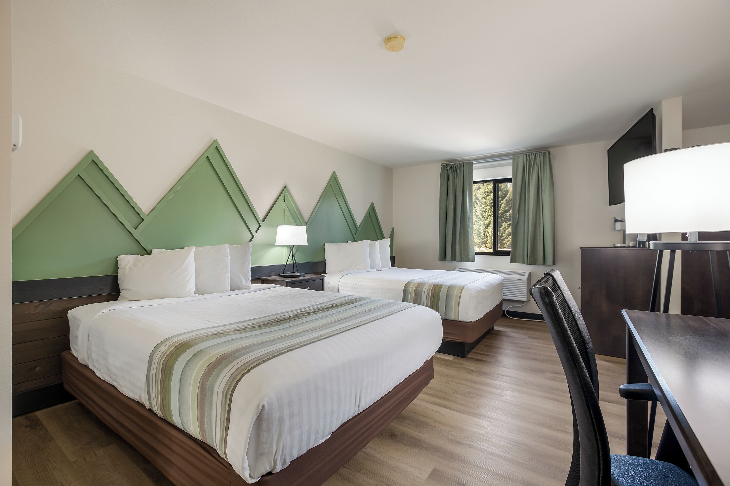 A hotel room with two beds, a desk, and a TV.