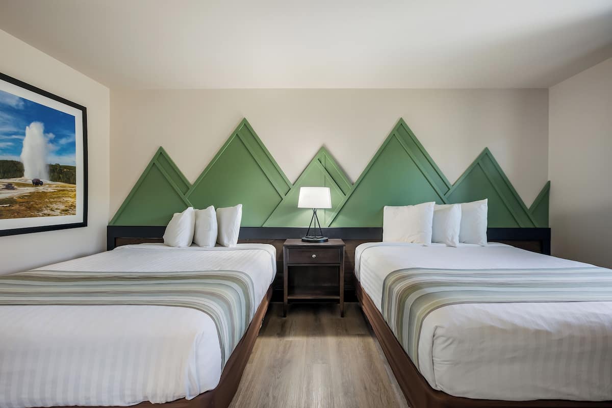 Hotelkamer met twee bedden, een nachtkastje met lamp, een lijst met afbeelding van een geiser en een groen geometrisch ontwerp op de muur.