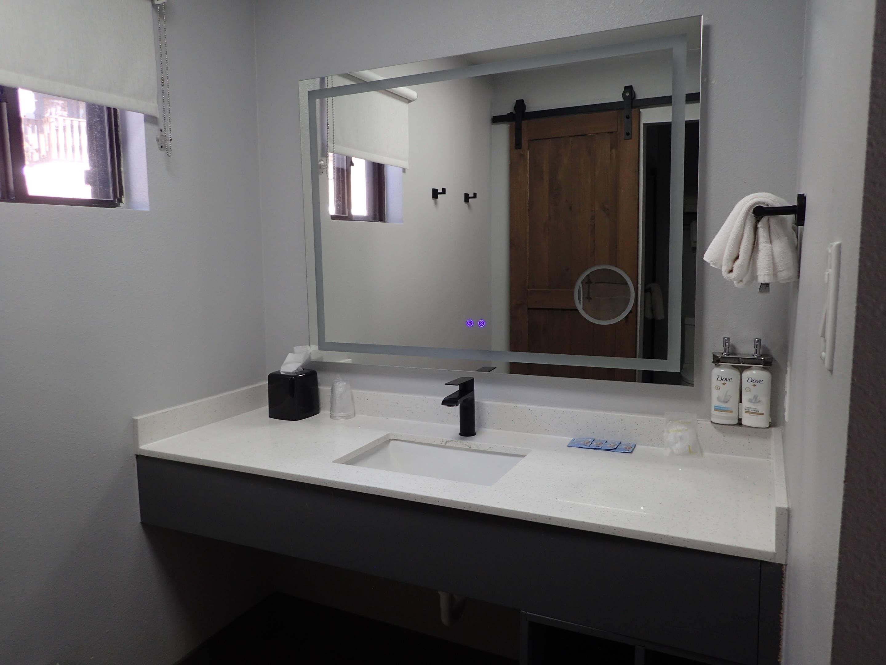 Un bagno con un lavandino bianco, uno specchio, un portascopino e sapone per le mani Dove.