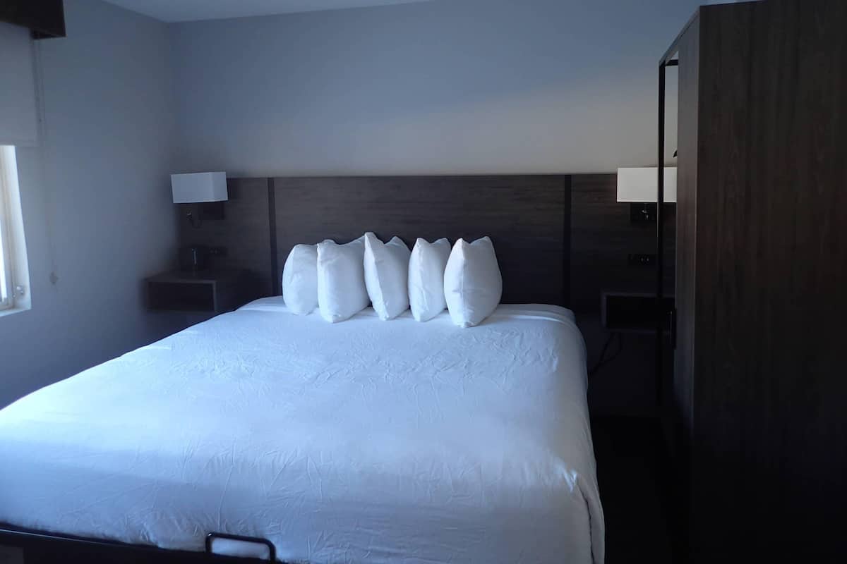 A hotel room with a large bed, a wooden headboard, a nightstand with a lamp, and a wardrobe.
