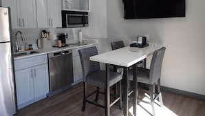 Cocina compacta con armarios blancos, microondas, cafetera y una mesa de comedor con sillas.