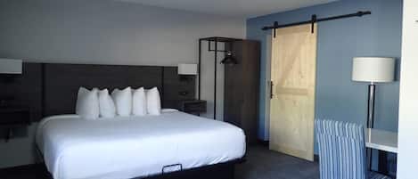 A modern hotel room with a large bed, bedside lamps, a wooden wardrobe, and a striped chair.