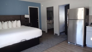 Una habitación de hotel con una cama grande, refrigerador, baño y kitchenette.