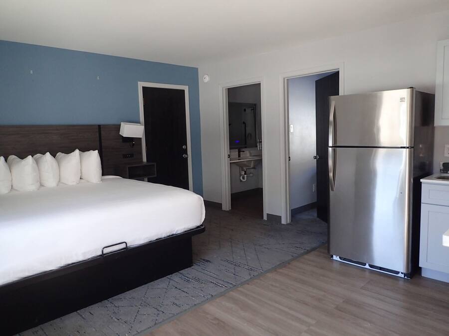 A hotel room with a large bed, a refrigerator, a bathroom, and a kitchenette.