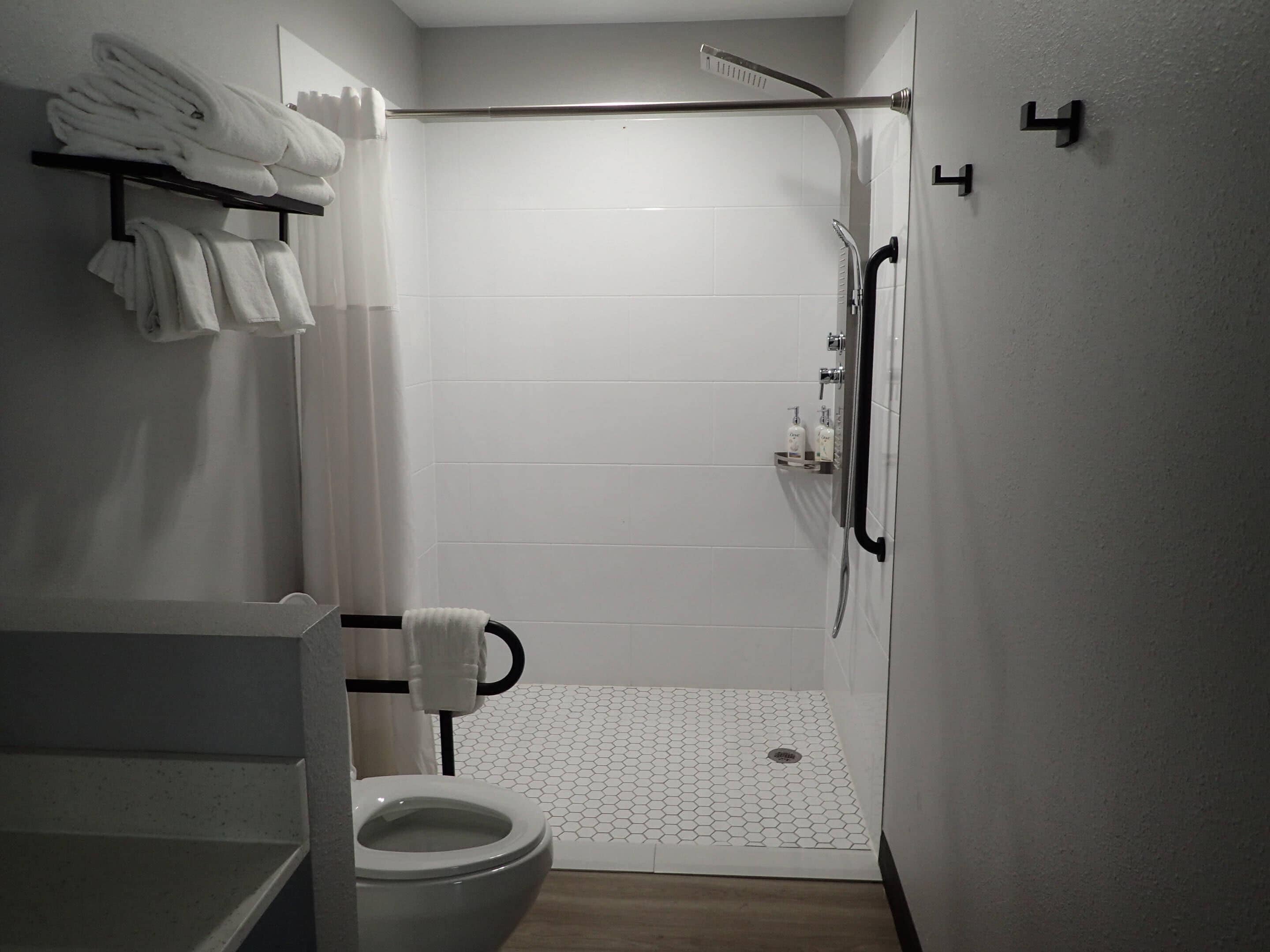 A modern bathroom with a shower, toilet, and neatly folded towels on a rack.