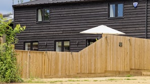 A two-story wooden house with a dark exterior, a wooden fence, and a small garden area. - The Old Dairy (Canterbury)