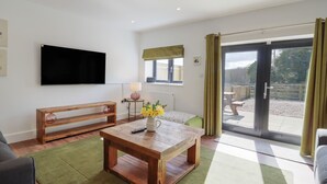 A living room with a wooden coffee table, a bench, a TV mounted on the wall, and a sliding glass door leading to an outdoor area. - The Old Dairy (Canterbury)