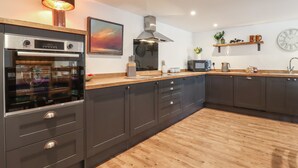 A modern kitchen with dark cabinets, a built-in oven, a microwave, and a wooden countertop. - The Old Dairy (Canterbury)