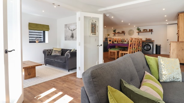 A modern living room with a grey sofa, wooden flooring, and a dining area with a table and chairs. - The Old Dairy (Canterbury)