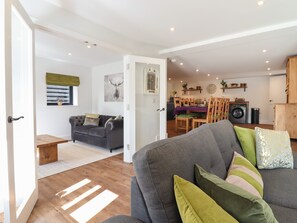 Una sala de estar moderna con un sofá gris, suelo de madera y una zona de comedor con mesa y sillas.