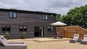 A modern log cabin with a patio area featuring a table and lounge chairs. - The Old Dairy (Canterbury)