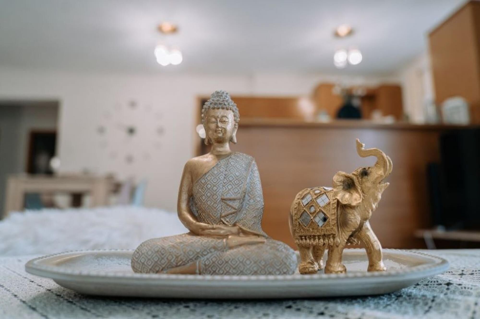 A Buddha statue on a tray with an elephant, in a room with a wooden cabinet and a white wall.
