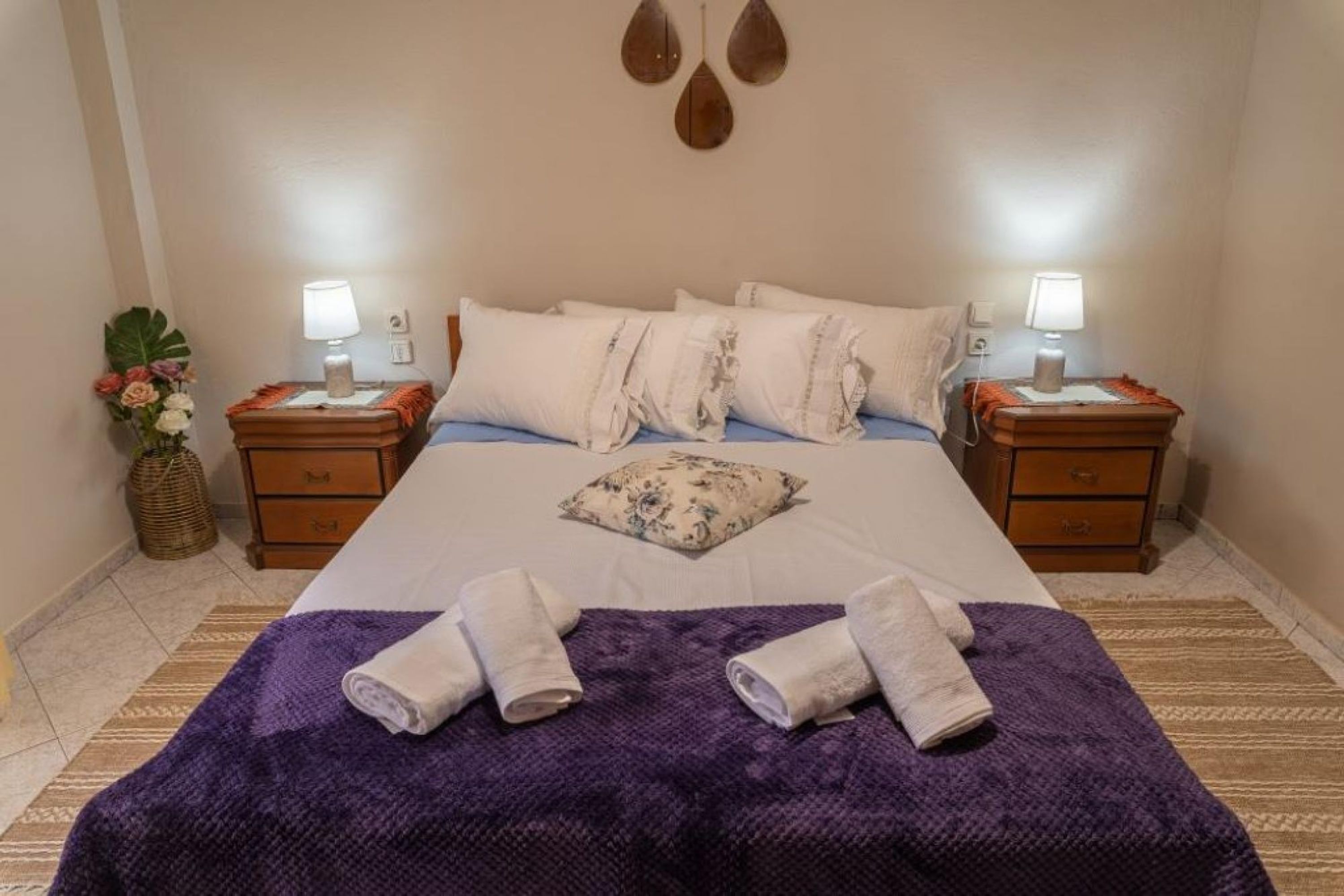 A neatly made bed with white linens, two bedside tables with lamps, a purple throw blanket, and a decorative pillow.