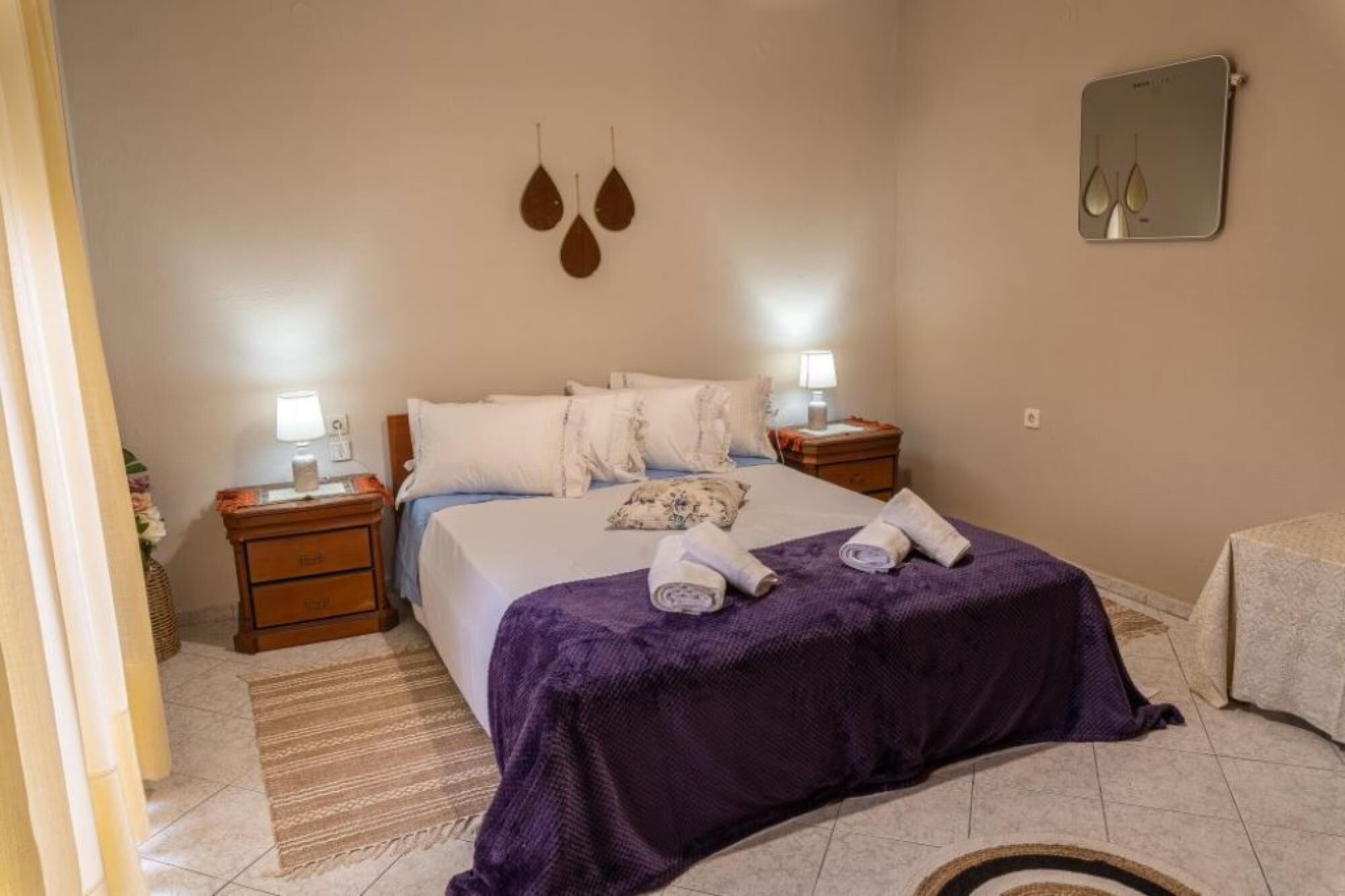 Een keurig opgemaakt slaapkamer met een bed, twee nachtkastjes, een spiegel en een paars plaid.