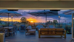 An outdoor deck with seating, umbrellas, and a view of the sunset. - Luxury Home with Pool/Spa/Sauna,Steps to the Beach (San Diego)