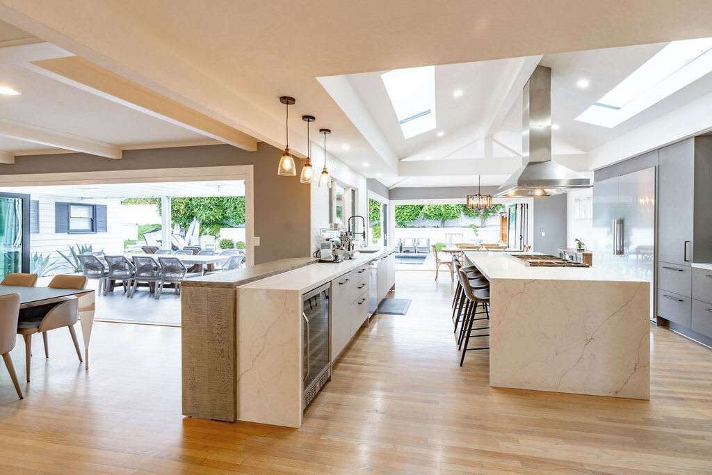 Een moderne keuken met een centraal eiland, een eethoek en grote ramen.