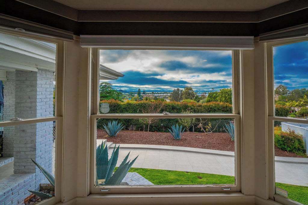 A room with a large window overlooking a landscaped garden and a distant view of a town.