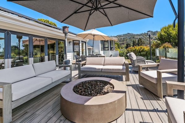 A deck with outdoor furniture, a fire pit, and a large umbrella.