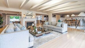A spacious living room with a fireplace, a sofa set, a coffee table, and a dining area with a chandelier. - Luxury Home with Pool/Spa/Sauna,Steps to the Beach (San Diego)