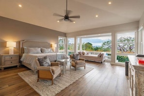 A spacious bedroom with a large bed, a ceiling fan, and a view of the outdoors through large windows.