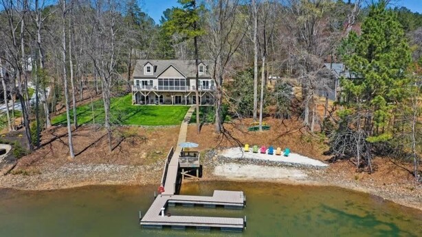 Una casa grande con un muelle que se adentra en un lago, rodeada de árboles.