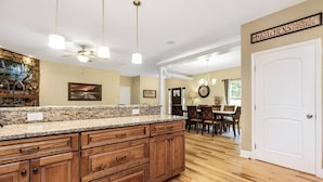 Una cocina con encimeras de granito, armarios de madera y un comedor con candelabro.
