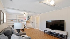 En moderne stue med et fladskærms TV, en sofa, en lampe og en trappe op til et repos.