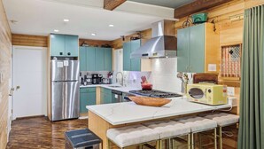 A kitchen with a stainless steel refrigerator, a stove, and a wooden island with bar stools.